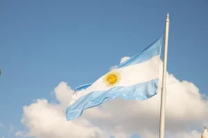 Foto da bandeira da Argentina tremulando num dia de céu azul com nuvens