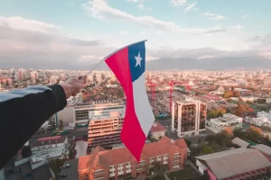 Bandeira do Chile sendo segurada por uma mão humana de frente para uma cidade