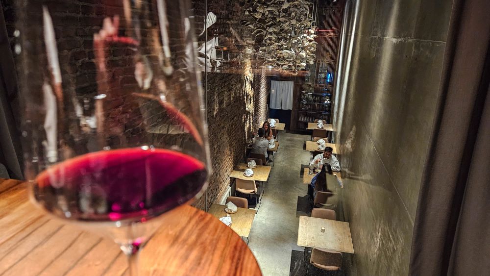 Interior do restaurante El Papagayo com ambiente contemporâneo e taça de vinho em primeiro plano.